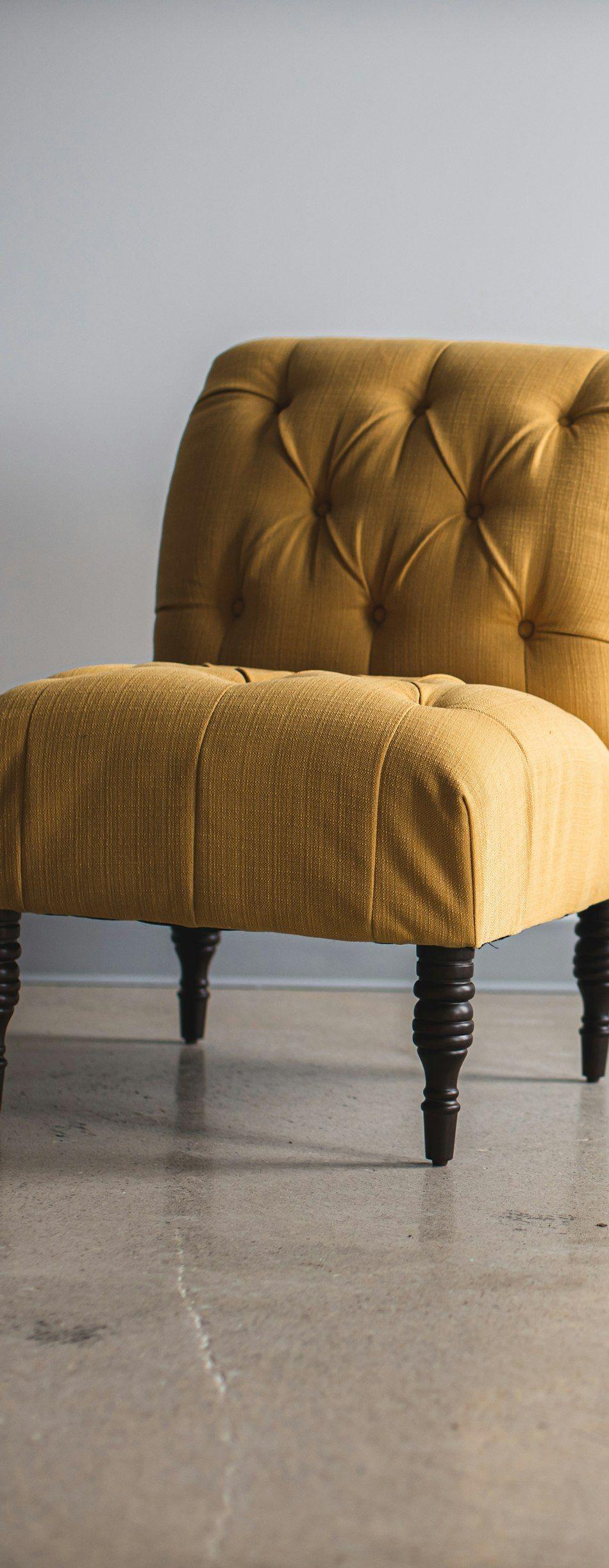 Mustard tufted slipper chair with turned dark-wood legs on a polished concrete floor