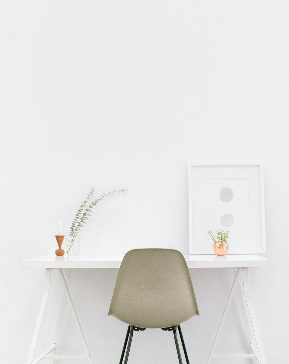 Minimal white workspace with a trestle desk, grey shell chair and framed print